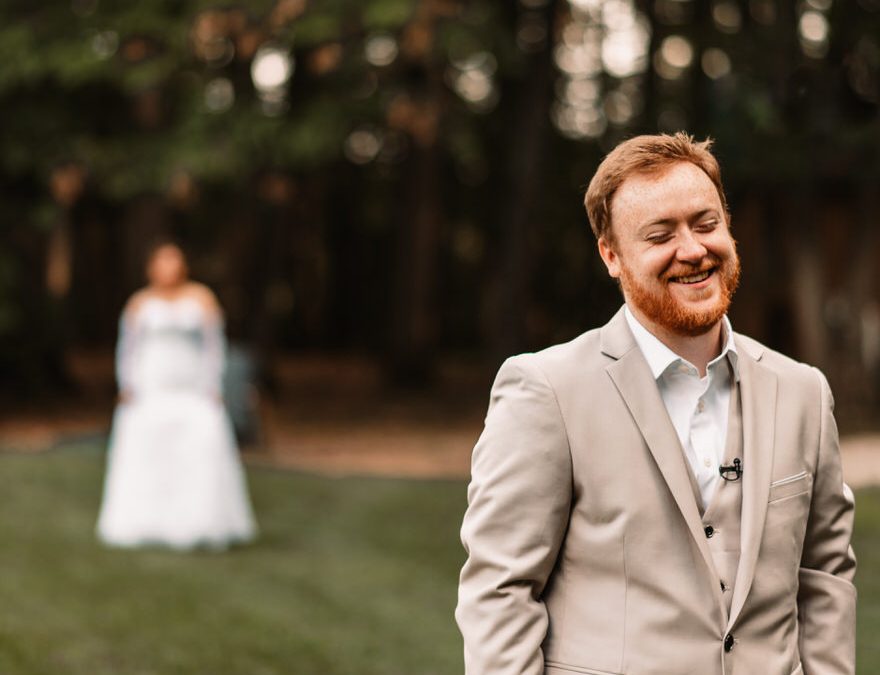 first look at a wedding outdoors bride in background close up groom