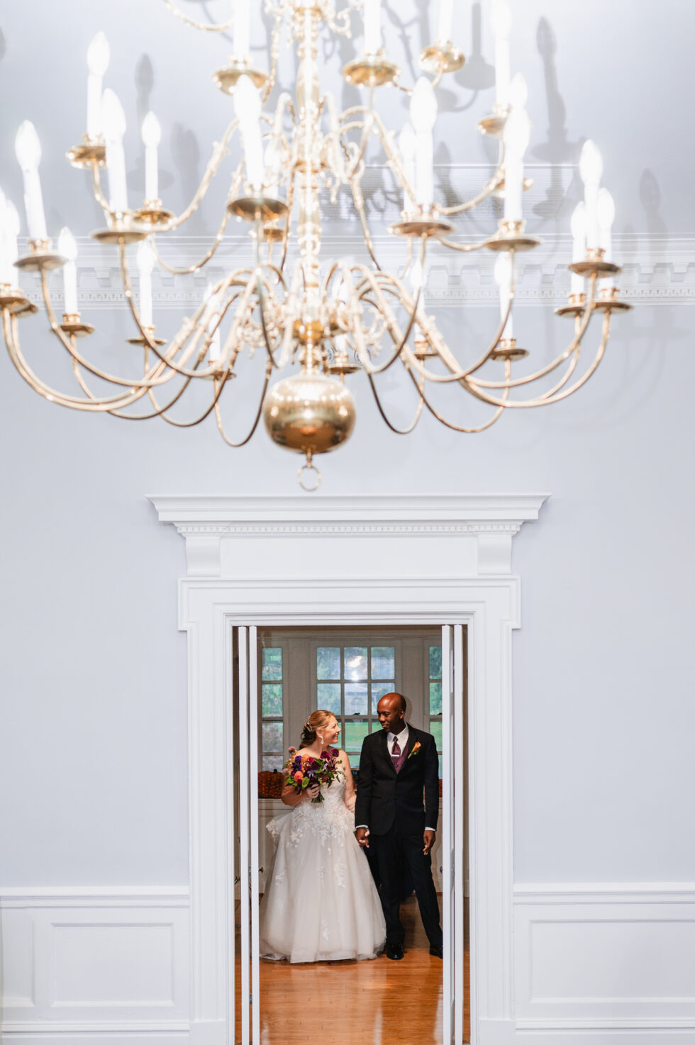 large chandelier hangs over a door where bride and groom enter their reception
