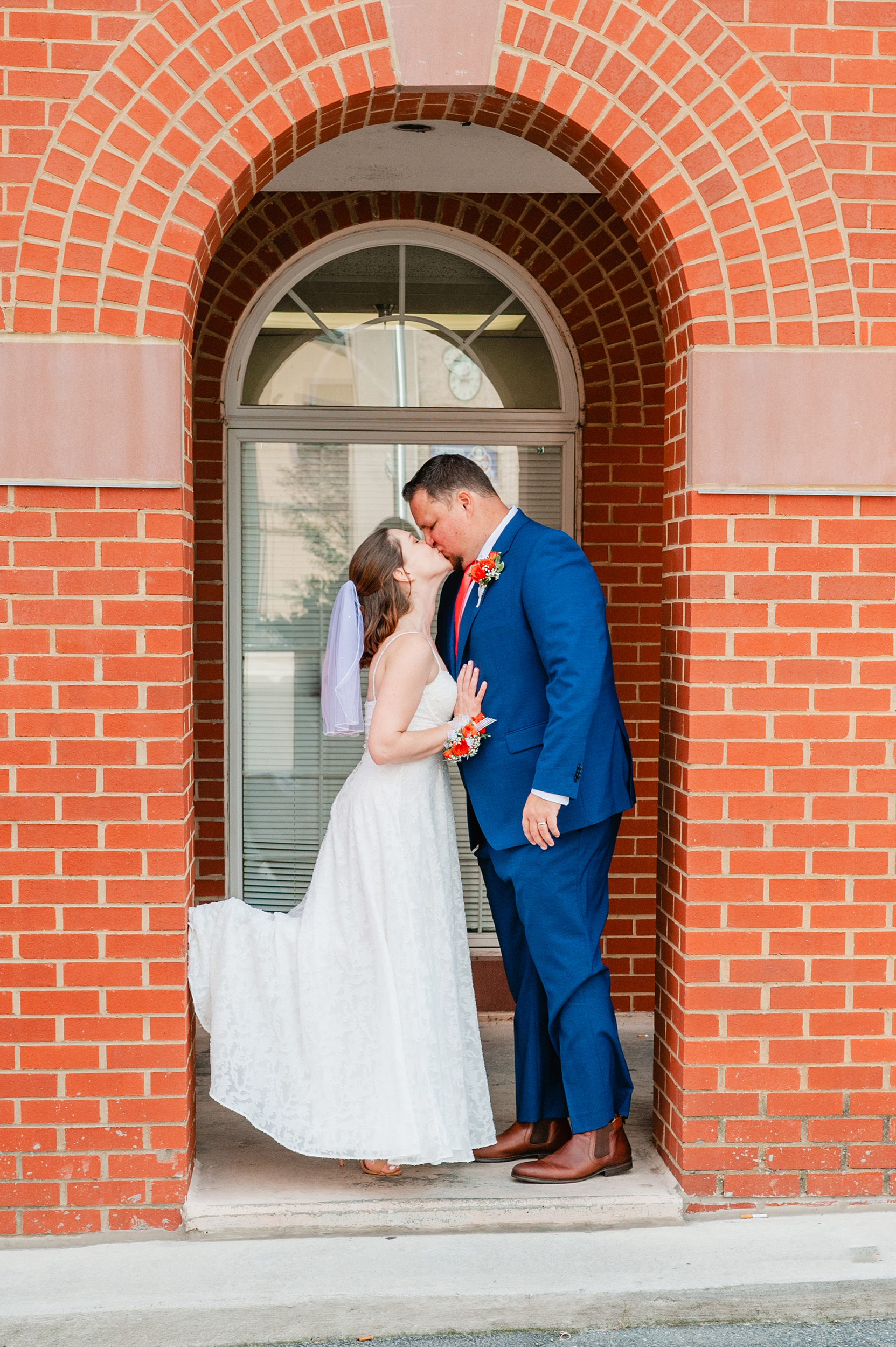 bride and groom kiss under a red brick archway