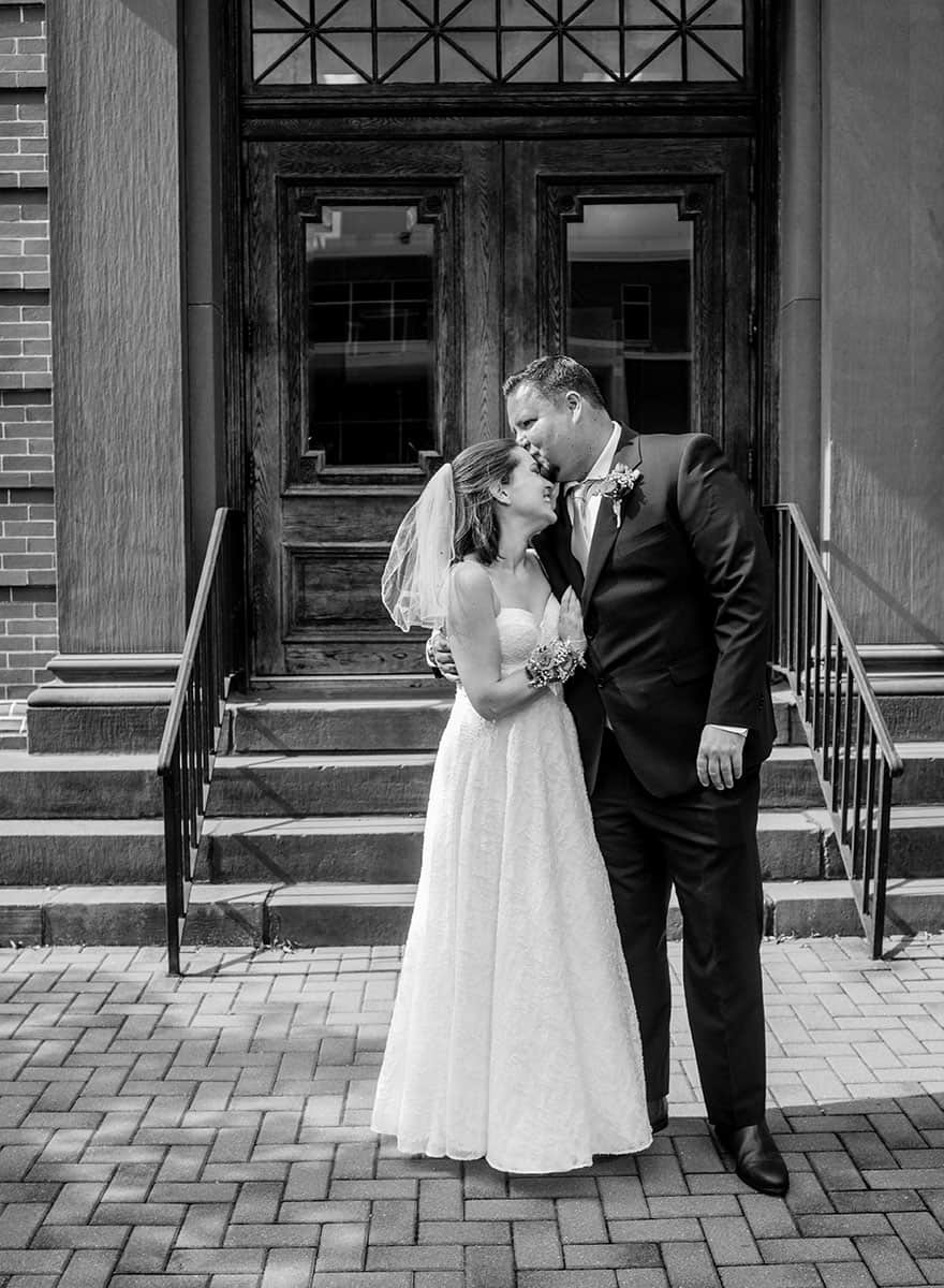 bride and groom kissing in front of doors in black and white