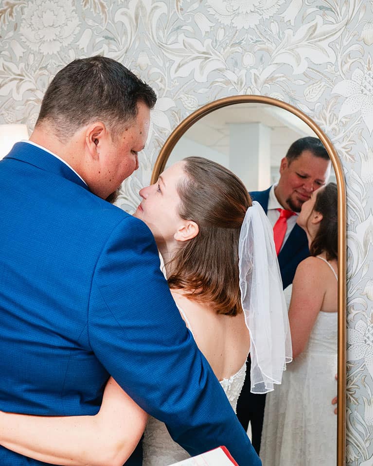 bride and groom standing in front of mirror looking at each other