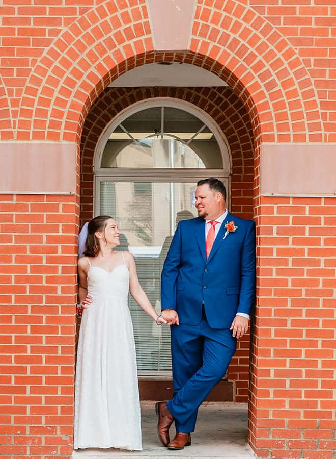 bride and groom looking at each other and holding hands in brick archway